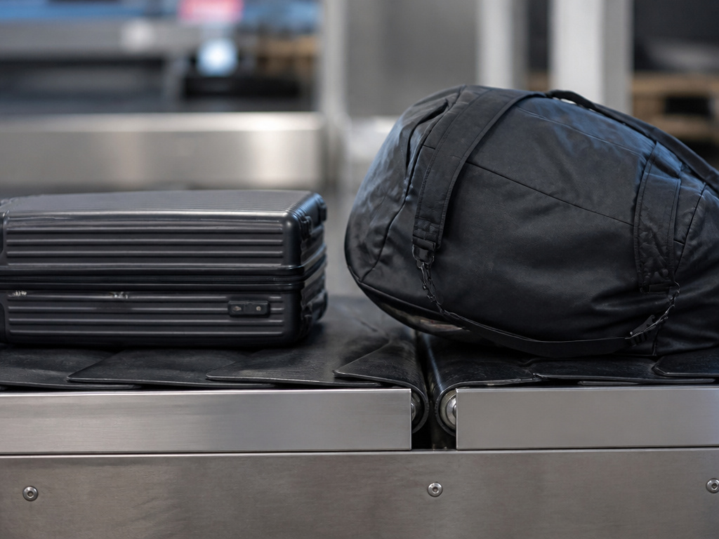 Structured carry-on luggage versus floppy duffel bag on airport conveyor belt system.